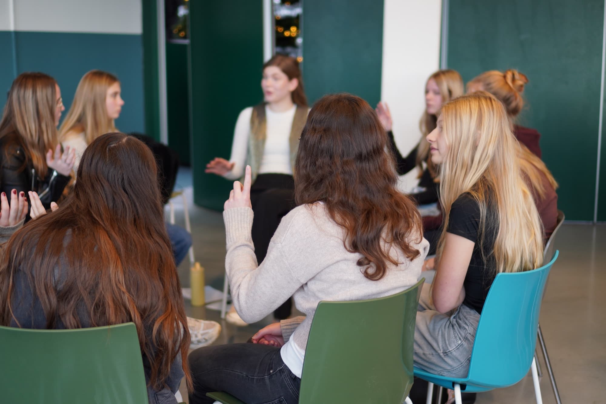 Een groep jongeren zit in een kring van stoelen met elkaar in gesprek tijdens een Kikid-sessie.